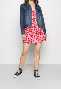 Röd blommig klänning med vita prästkragar, lager på lager under en mörk denimjacka. Svarta högskor fulländar outfiten.