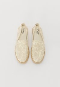 Béžové espadrilky s komplexnou kvetinovou výšivkou, elastickými bočnými panelmi a opletenými juty podrážkami, s nápisom "TOMS" vo vnútri.