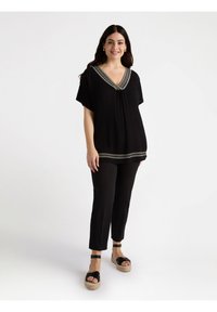 Tunic nera con maniche corte e scollatura a V, caratterizzata da un bordo decorativo in argento. Abbinata a pantaloni neri e sandali platform neri con cinturini.
