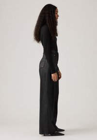 Zwarte langemouwen top gecombineerd met hoge taille, wijde zwarte denim broeken. De outfit heeft een minimalistisch ontwerp en een strakke textuur.