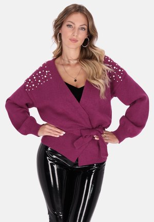 Cardigan a magenta con design avvolgente, caratterizzato da dettagli in perle sulle spalle, abbinato a leggings neri lucidi.