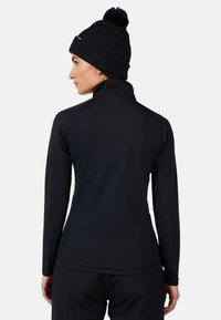 Maglietta nera a maniche lunghe con colletto alto, design aderente, texture liscia e cuciture visibili; completata da un berretto nero a maglia con pom-pom.