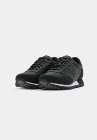 Zwarte sportieve schoenen met een mix van gladde en gestructureerde materialen, met een ronde neus, vetersluiting aan de voorkant en witte accenten op de middenzool.