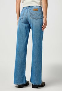 Jean flare de mezclilla azul clara con cintura alta, que cuenta con bolsillos traseros y una etiqueta de cuero. La textura es suave con un ligero desgastado.
