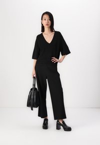 Top de malha preto com decote em V, combinado com calças largas pretas. Realçado com uma bolsa tote preta e sapatos com salto grosso pretos.