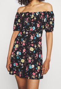 Czarna sukienka w kwiaty z bufkami na krótkich rękawach, dekoltem odsłaniającym ramiona oraz kolorowymi wzorami kwiatów w różowym, niebieskim i żółtym kolorze.