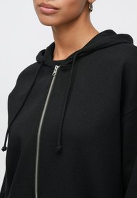 Felpa nera con zip integrale e cappuccio regolabile con coulisse, realizzata in tessuto morbido. Presenta una zip argentata e una vestibilità comoda.