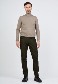 Beige kauluspaidan villatakki ja tummanvihreät slim-fit-housut, jotka on valmistettu teksturoidusta kankaasta, yhdistetty mustiin kenkiin. Yksinkertainen muotoilu, neutraalit värit.