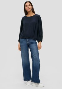 Marineblaues, strukturiertes Langarmoberteil kombiniert mit weit geschnittenen blauen Jeans und weißen Plateau-Sneakern. Lässiges Outfit mit lockerer Passform.