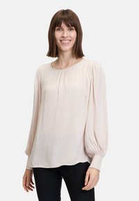Blusa rosa chiaro con maniche lunghe e puffate e scollatura arricciata. Tessuto leggero e morbido con una trama liscia e una vestibilità comoda.