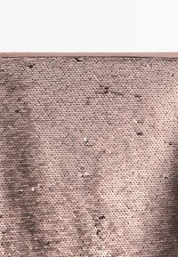 Gros plan d’un tissu couvert de petits sequins ronds couleur or rose, disposés en rangées serrées et chevauchantes.