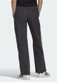 Svarta byxor med vida ben och en slät yta, med bakfickor och en kontrasterande sidremsa. Bärs med vita sneakers.