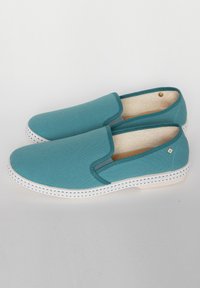 Teal canvas instapschoenen met een gestructureerd oppervlak, witte rubberen zool en blauwe accentstiksels. Minimalistisch ontwerp zonder sluitingen.