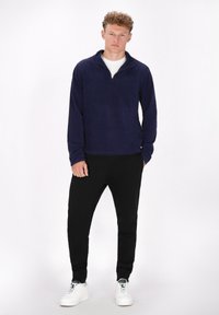 Pullover in pile blu navy con colletto e mezza zip, abbinato a pantaloni della tuta neri e sneakers bianche. Texture liscia, vestibilità comoda.