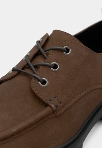 Smeđa cipele od antilopa s vezicama i crnim gumenim potplatom, krupni plan na rupice za vezice i detalje šavova.