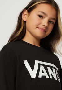 Sort bomulds langærmet skjorte med et fremtrædende hvidt "VANS" logo. Glat tekstur med klassisk rund hals.