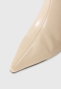 Pointed beige leather shoe toe with visible stitching on a white background.
