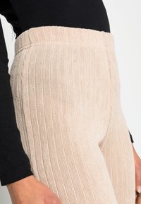 Leggings rosa claro com textura canelada e cintura elástica, combinados com uma blusa preta de mangas longas.