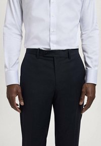 White striped long-sleeve shirt paired with dark slim-fit trousers, featuring a button closure, belt loops, and clean crease down the front.