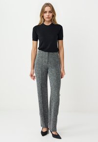 Top corto nero a maniche corte abbinato a pantaloni grigi a vita alta con motivo. I pantaloni presentano un design a gamba larga e una sottile texture. Scarpe nere a punta.