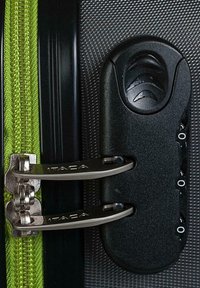 Candado de maleta negra con dos cremalleras plateadas, tirador de cremallera verde y una superficie texturizada negra y gris con el nombre de la marca "ITACA" visible.