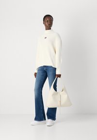 White, ribbed sweater with high neckline, blue flared jeans, white sneakers, and a cream handbag with a zipper and shoulder strap.
