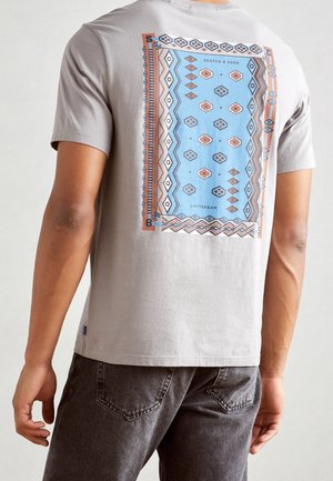 Grey cotton t-shirt featuring a blue geometric pattern with red and brown accents on the back. Short sleeves and a relaxed fit.