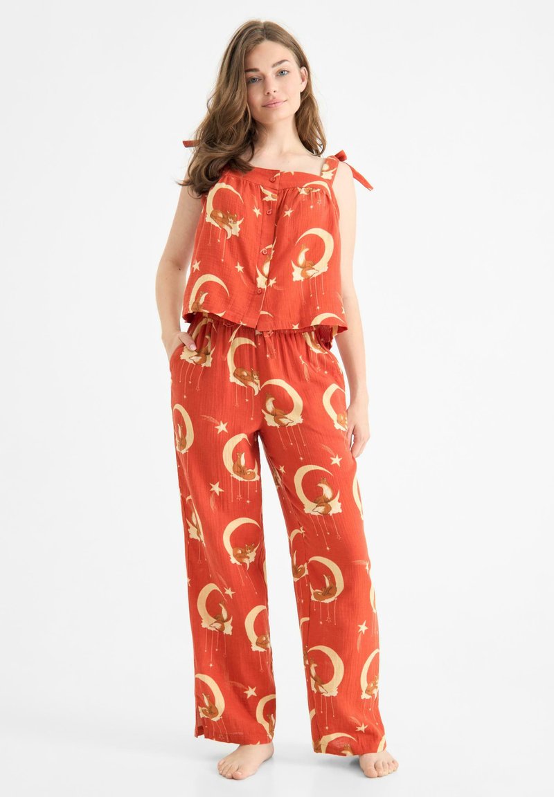 Conjunto de dos piezas rojo que presenta una blusa sin mangas con tirantes de lazo y pantalones estampados con lunas y estrellas. Fabricado en tela ligera.