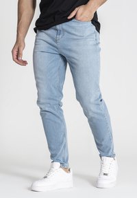 Jeans de mezclilla azul claro con un corte ajustado, que presentan una textura suave y un diseño minimalista. Combinados con zapatillas blancas.