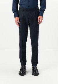 Pantaloni de costum navy dintr-un material neted, cu o croială ajustată, având un sistem frontal plat și curea, asortați culoaferi negri.