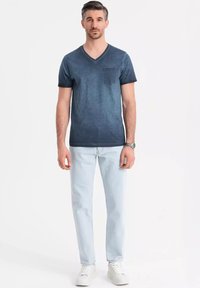 T-shirt da uomo blu scuro a V con taschino, abbinato a jeans azzurri e sneaker bianche. Tessuto morbido, vestibilità casual, design minimale.