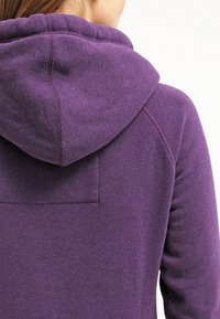 Sudadera morada con un acabado texturizado, que cuenta con una capucha con cordón y un pequeño bolsillo en la parte trasera. Diseño suave y casual.