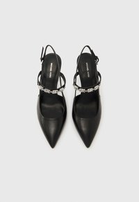 Escarpins à talons avec bride arrière en cuir noir, bouts pointus et brides ornées d'accent argenté. Texture lisse et design minimaliste, avec une semelle intérieure de marque.