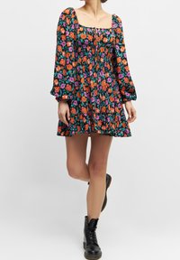 Robe noire à motifs floraux avec manches longues bouffantes, décolleté carré et taille froncée. Portée avec des bottes noires lacées.