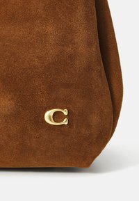 Bruine suède handtas met een zachte textuur en een gouden C-logo accent aan de zijkant. Compakte vorm met zachte randen.