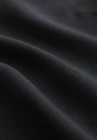 Tissu noir texturé avec une surface lisse et légèrement réfléchissante, mettant en valeur des plis doux et une profondeur subtile dans la couleur et la texture.
