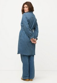 Abito in denim con vita stretta, maniche lunghe e colletto. Di lunghezza media e vestibilità comoda, presenta una texture liscia e blu.