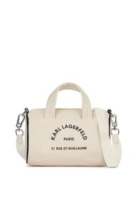 Vászons kézitáska világos bézs színben fekete mintával. Két fogantyúval és levehető vállpánttal rendelkezik. A szöveg tartalmazza a márka és a cím részleteit.