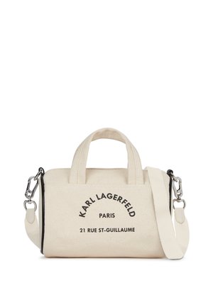 Vászons kézitáska világos bézs színben fekete mintával. Két fogantyúval és levehető vállpánttal rendelkezik. A szöveg tartalmazza a márka és a cím részleteit.