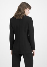 Black tailored blazer with long sleeves, structured design, and a smooth texture. Features a back seam and a modern, minimal silhouette.