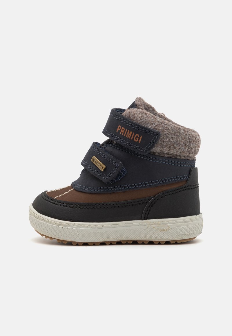 Botte marron et marine avec col en feutre gris, bandes Velcro, semelle en caoutchouc et détails en surpiqûre. Conçue pour la durabilité et le confort.