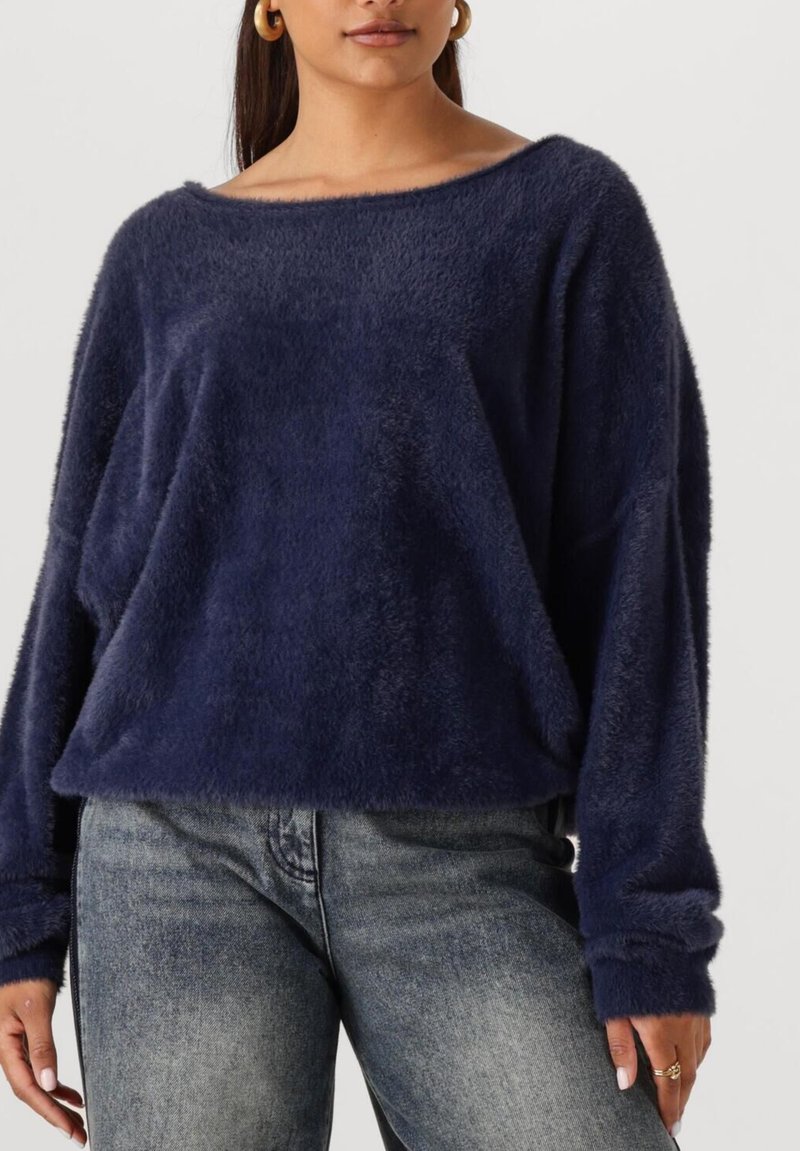 Marineblauwe, fuzzy pullover trui met een off-the-shoulder halslijn en lange mouwen, gecombineerd met licht versleten grijze jeans.