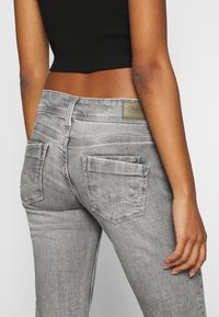 Jeans de mezclilla gris con un diseño ajustado, que cuentan con bolsillos traseros, detalles de costura sutiles y una etiqueta de marca en la cinturilla.