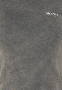 Ciemnoszara bawełniana koszulka z ryflowaną strukturą. Zawiera biały haftowany napis "iets trans..." umieszczony z przodu.