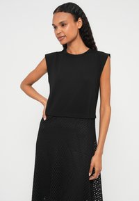Čierny bezrukávový krátky top s okrúhlym výstrihom, vyrobený z hladkej tkaniny, doplnený o štruktúrovanú čiernu sukňu s vzorovaným dizajnom.