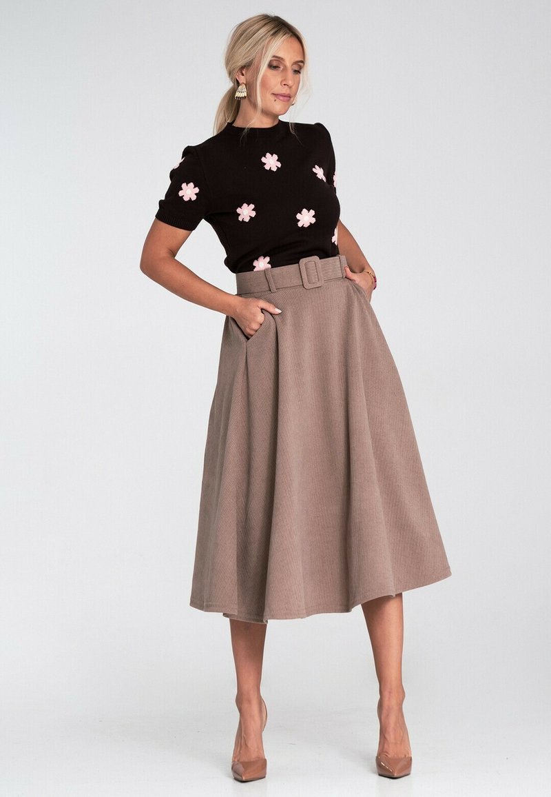 Czarny sweter z krótkim rękawem z różowym haftem kwiatu, w połączeniu z beżową spódnicą plisowaną z wysokim stanem z paskiem i kieszeniami.