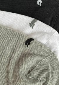Drei Paar Socken: schwarz, weiß und grau, mit kleinen gestickten Tierlogos. Die Textur ist glatt und gestrickt.