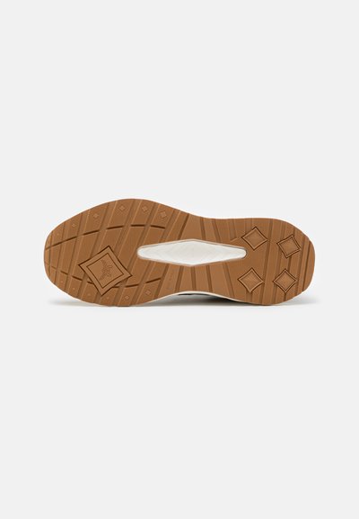 Semelle d'une sneaker avec une semelle en caoutchouc marron arborant des motifs en diamants et des rainures, et une semelle intermédiaire blanche avec un détail découpé.