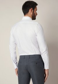 Biała koszula z długim rękawem i klasycznym kołnierzem, zestawiona z szarymi, dopasowanymi spodniami z dwoma tylnymi kieszeniami i ozdobnymi guzikami.