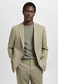 Lichtbeige pak met een gestructureerde blazer, bijpassende broek, en een grijze gebreide trui. Glad stof, op maat gemaakt pasvorm, en goudkleurige knopen.